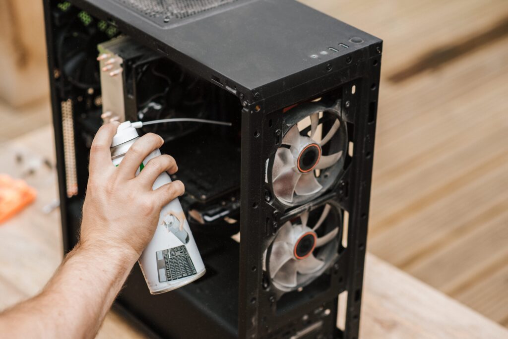 Person using a can of compressed air to clean dust from a computer system